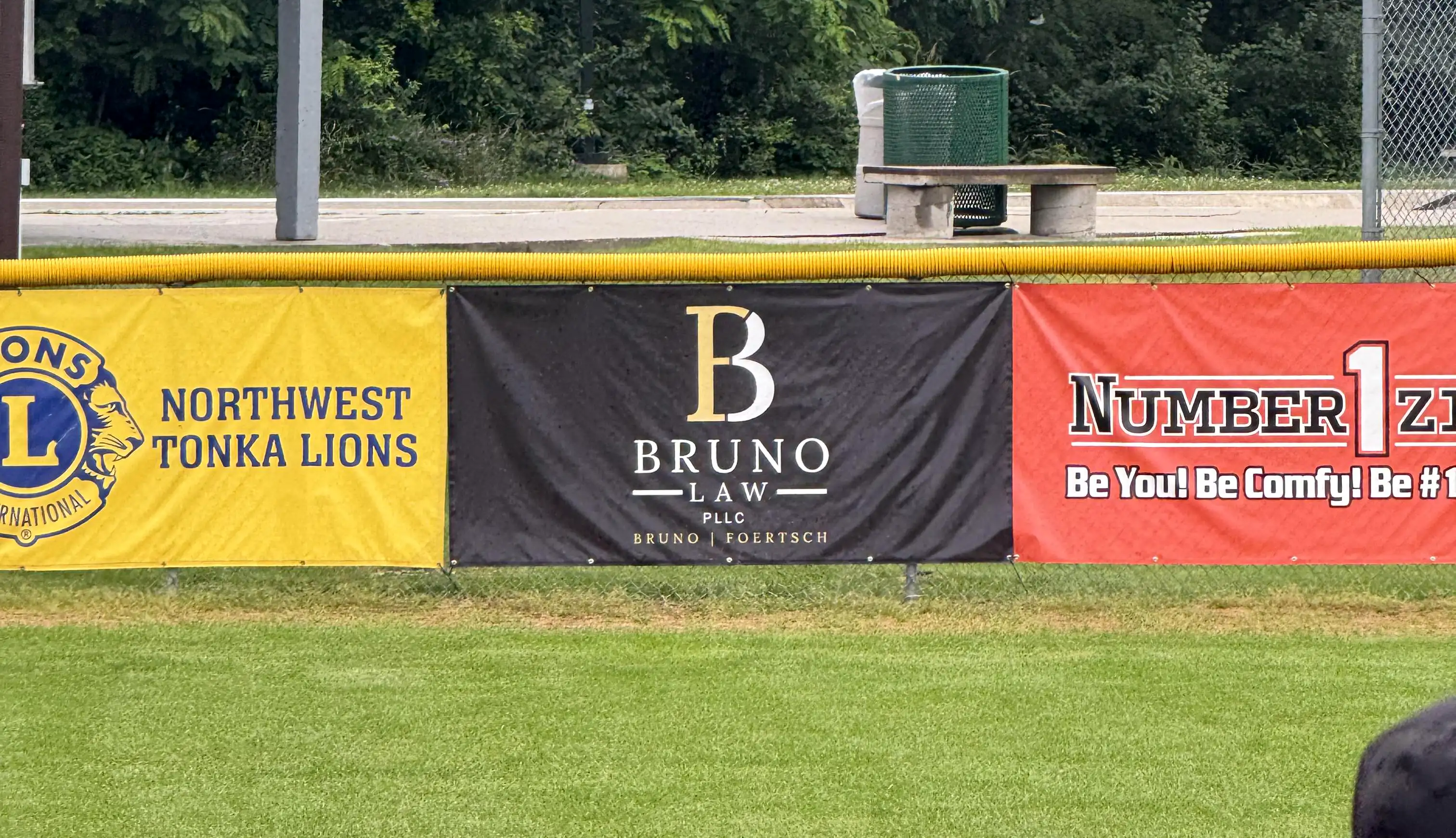 Bruno Law sponsor banner on the outfield fence at a Westonka youth baseball field